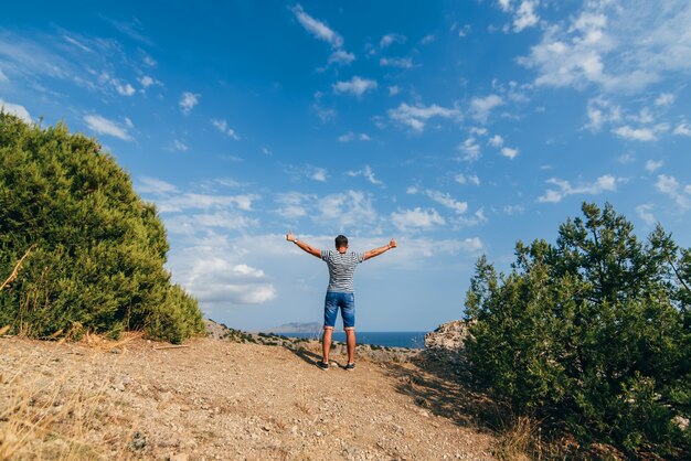 Male traveler with arms raised to sky on top of mountain