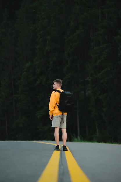 山の森の風景の道の真ん中に立っている黄色のスウェットシャツの男性旅行者