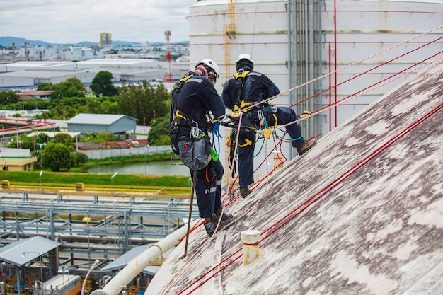 タンク屋根の高所で作業するセーフティーファーストハーネスロープセーフティーラインを装着した男性2人作業員検査 球形