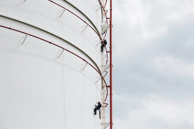 Male two workers control rope down height tank rope access\
inspection of thickness shell plate storage tank safety work at\
height.