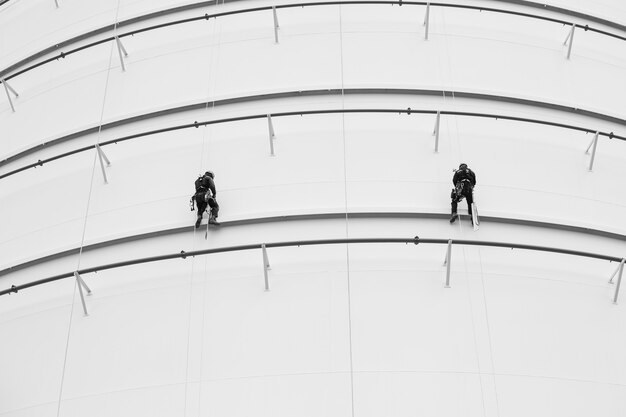 Male two workers control rope down top roof tank rope access inspection of thickness shell plate storage tank gas safety work at height.