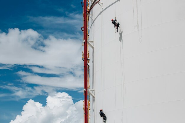 Male two workers control swing rope down height tank rope
access inspection of thickness pipeline and tank gas in the blue
sky.