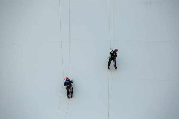 Мужчины два рабочих вниз по высоте резервуар веревочный доступ осмотр толщины оболочки пластинчатого резервуара для хранения газа пропана безопасность работы на высоте.