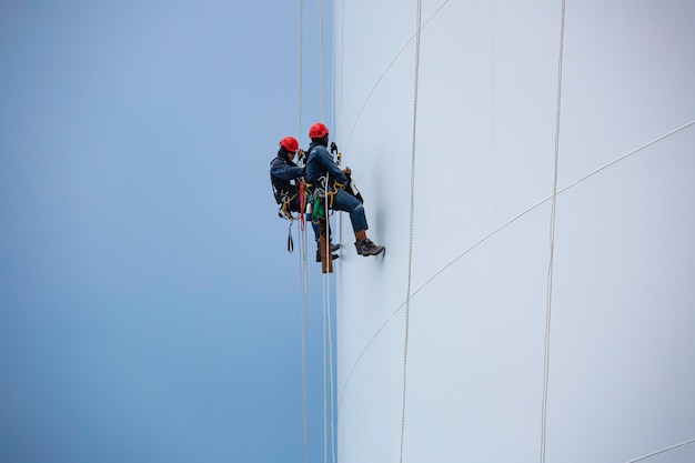 Мужчины два рабочих вниз по высоте резервуар веревочный доступ осмотр толщины оболочки пластинчатого резервуара для хранения газа пропана безопасность работы на высоте.