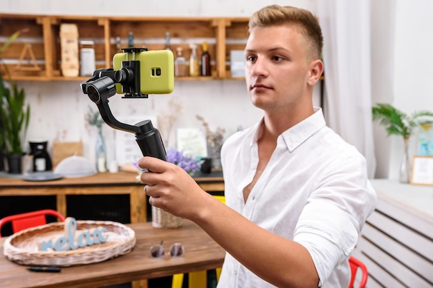 Мужчина-блогер фотографирует себя на камеру со стабилизатором. Съемка видеоблога на кухне