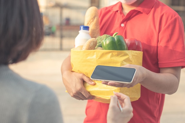 家のポーチで食料品を保持している男性のボランティアフェイスマスクと手袋で配達の女性