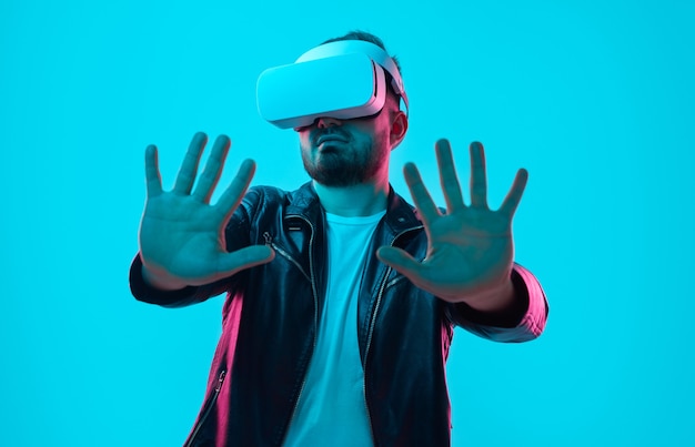 Male in VR headset interacting with virtual reality with outstretched arms in studio with neon lights on blue background