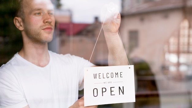 Male waiter putting on welcome sign on coffee shop window