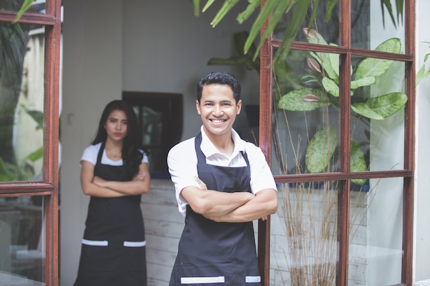 Male waiter standing with arms crossed in cafe