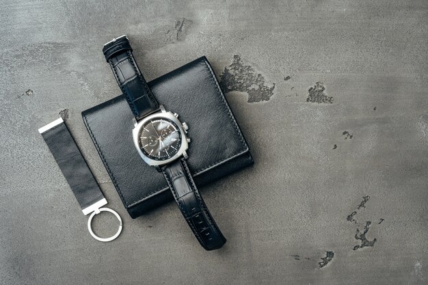 Male watch and leather wallet on dark grey surface close up