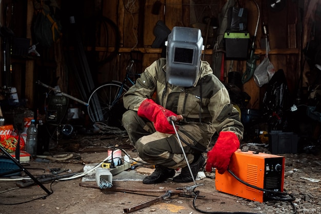 A male welder in a welding mask works with an arc electrode in his garage. Welding, construction, metal work.