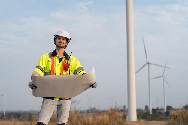 Male windmill engineer holding blueprint to inspection and maintenance of wind turbine in wind farm