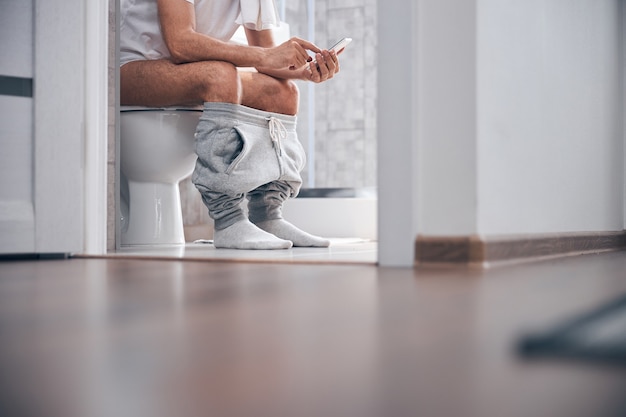  male with a cellular phone sitting on the toilet seat