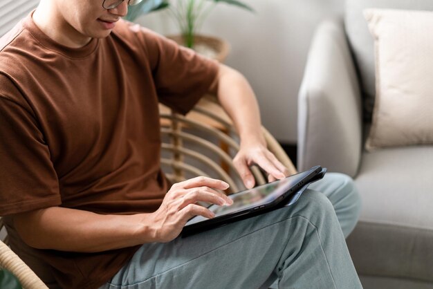 The male with his casual and jeans sitting comfortably on the wooden chair and doing touchscreen