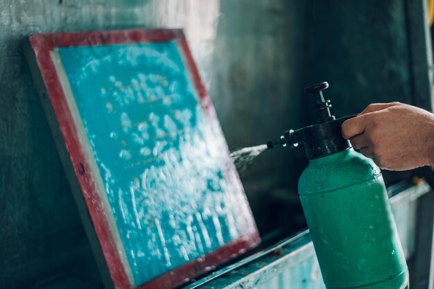 Male worker cleaning screen frame with water in a printing
workshop