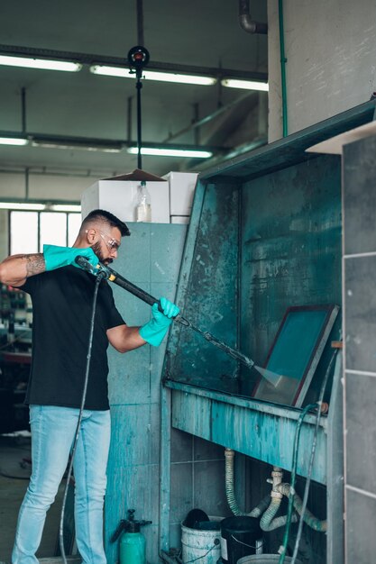 Male worker cleaning screen frame with water in a printing
workshop