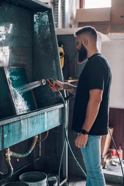 Male worker cleaning screen frame with water in a printing\
workshop