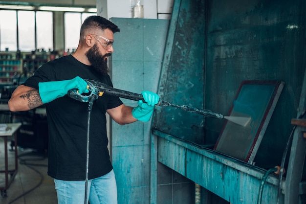 Male worker cleaning screen frame with water in a printing\
workshop