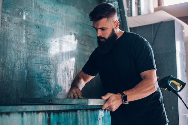 Male worker cleaning screen frame with water in a printing workshop