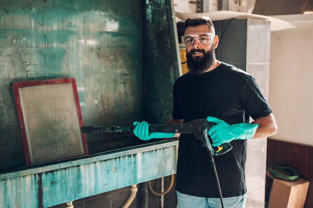 Male worker cleaning screen frame with water in a printing\
workshop