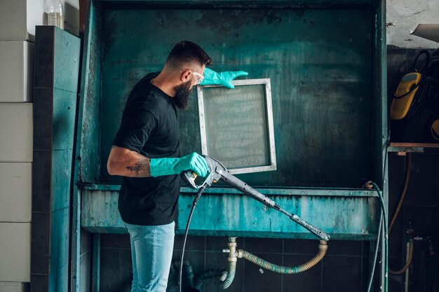 Male worker cleaning screen frame with water in a printing\
workshop