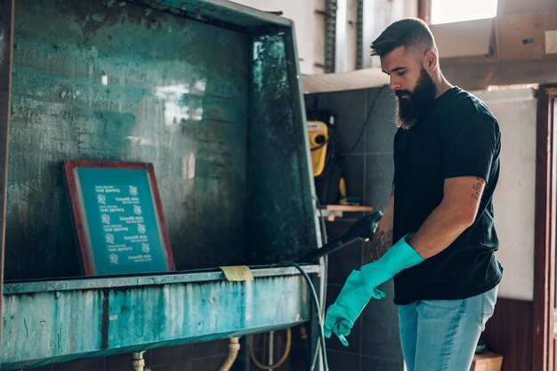 Male worker cleaning screen frame with water in a printing\
workshop