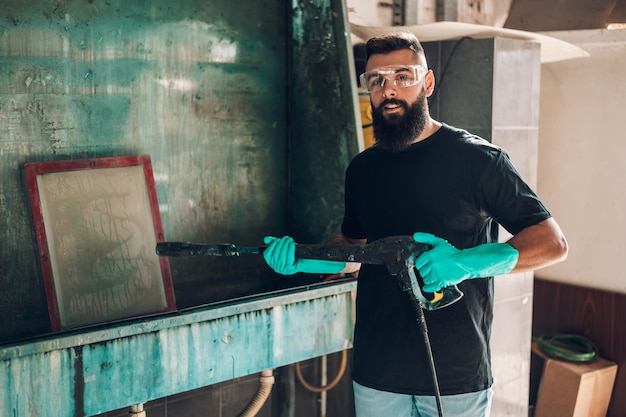 Male worker cleaning screen frame with water in a printing
workshop