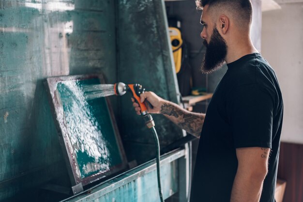 Male worker cleaning screen frame with water in a printing\
workshop