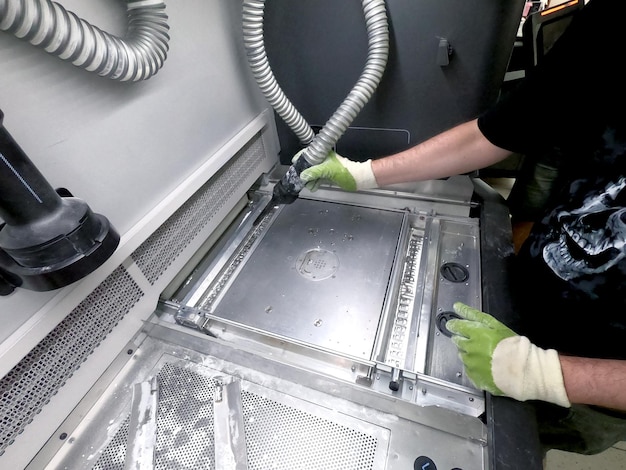 A male worker cleans the surface of an industrial 3D printer from white powder