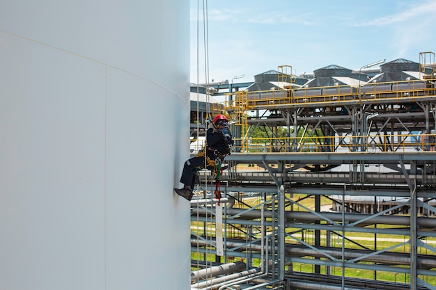 Foto lavoratore di sesso maschile in basso altezza serbatoio shell piastra scala di corda accesso ispezione di sicurezza del gas propano del serbatoio di stoccaggio di spessore.