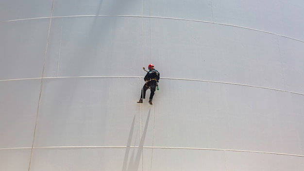 Male worker down height tank shell plate rope ladder  access safety inspection of thickness storage tank gas propane.