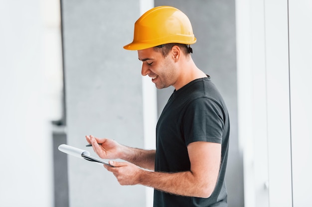 Male worker or engineer in yellow hard hat standing indoors with notepad