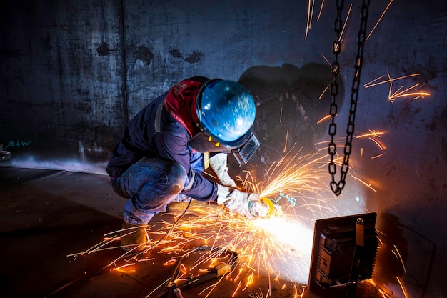 Мужчина-работник шлифует стальную пластину со вспышкой искр крупным планом в замкнутых пространствах.