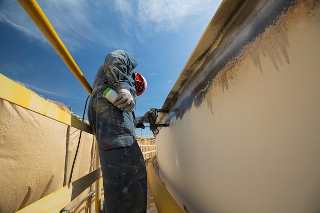 A male worker at high test steel tank butt weld overlay carbon shell plate of storage tank oil background white contrast of magnetic field test