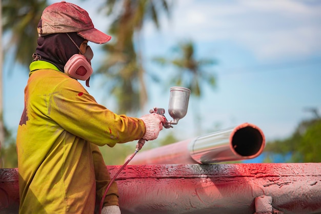 Male worker holding industrial size spray gun used for pipeline surface painting