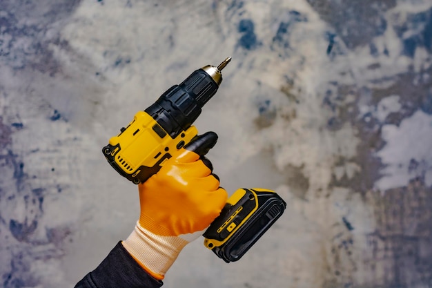 Male worker holds a closeup electric cordless screwdriver in his hands against the background of a construction tool and a concrete wall