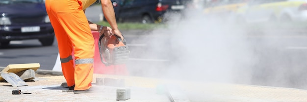 Il lavoratore maschio tiene la taglierina del gas nelle sue mani e taglia il cemento. concetto di lavori stradali di costruzione