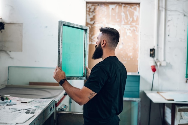 Male worker holds the silkscreen frame in a printing\
workshop