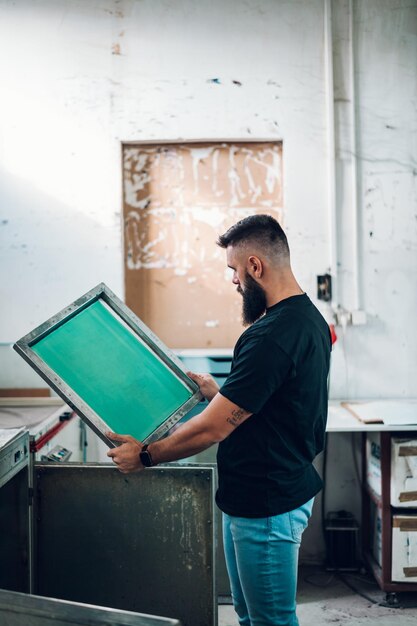 Photo male worker holds the silkscreen frame in a printing workshop