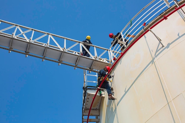 Male worker industrial rope access welder working at height\
wearing harness, helmet safety equipment rope access inspection of\
thickness storage tank industry.