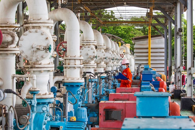 Male worker inspection pump motor oil at steel long pipes and pipe elbow in station oil factory during refinery valve of visual check record pipeline