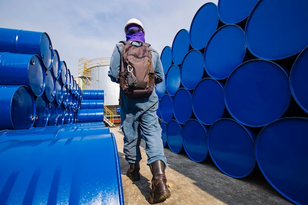 Мужчина-рабочий осматривает бочки с нефтью в бочках синего цвета, горизонтальные или химические