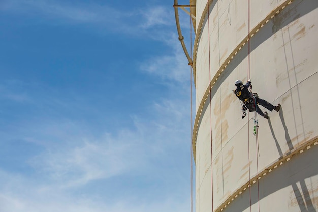 Male worker inspection wearing safety first harness rope safety\
line working at a high place on tank roof spherical gas blue\
sky