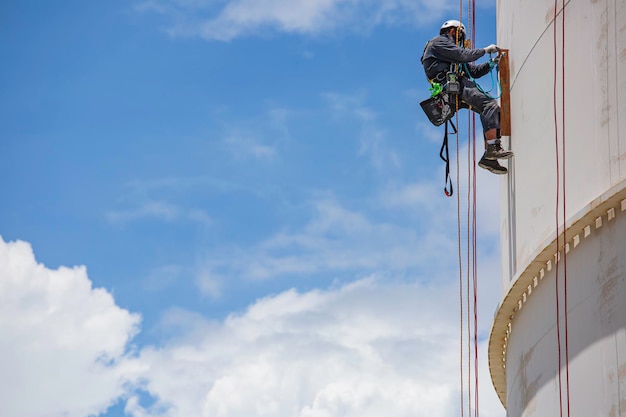 Male worker inspection wearing safety first harness rope safety\
line working at a high place on tank roof spherical gas blue\
sky