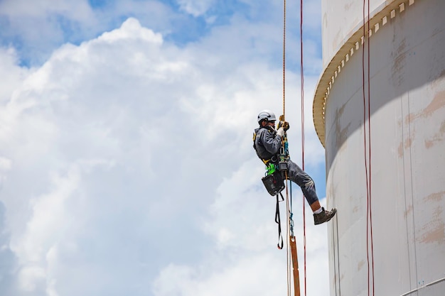 Male worker inspection wearing safety first harness rope safety line working at a high place on tank roof spherical gas blue sky