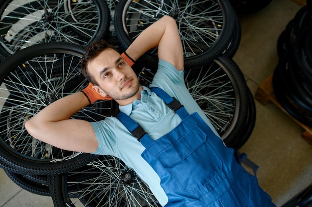 Lavoratore di sesso maschile che si trova sulla pila di ruote di bicicletta in fabbrica. linea di assemblaggio cerchi bici in officina, installazione componenti ciclo, tecnologia moderna