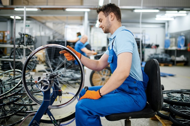 工作機械の男性労働者が工場で自転車のリムをチェックします。ワークショップでの自転車の車輪の組み立て