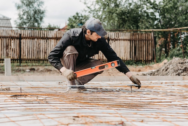 male worker measures the construction level of rebar for foundation of a house under construction