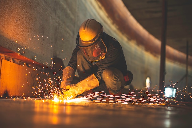 Male worker metal cutting spark on tank bottom steel plate with flash of cutting light close up wear protective gloves and mask in side confined space.