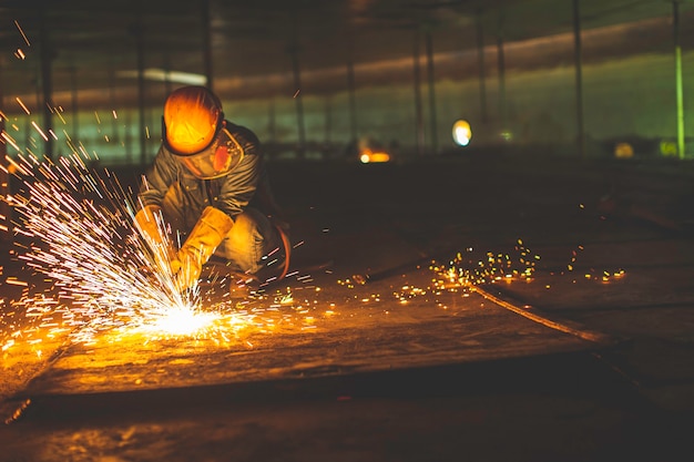 Male worker metal cutting spark on tank bottom steel plate with flash of cutting light close up wear protective gloves and mask in side confined space.